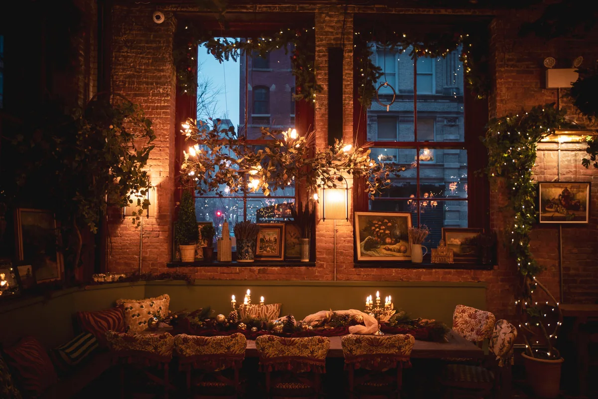 Candlelit dinner table set beneath garlanded windows at dusk